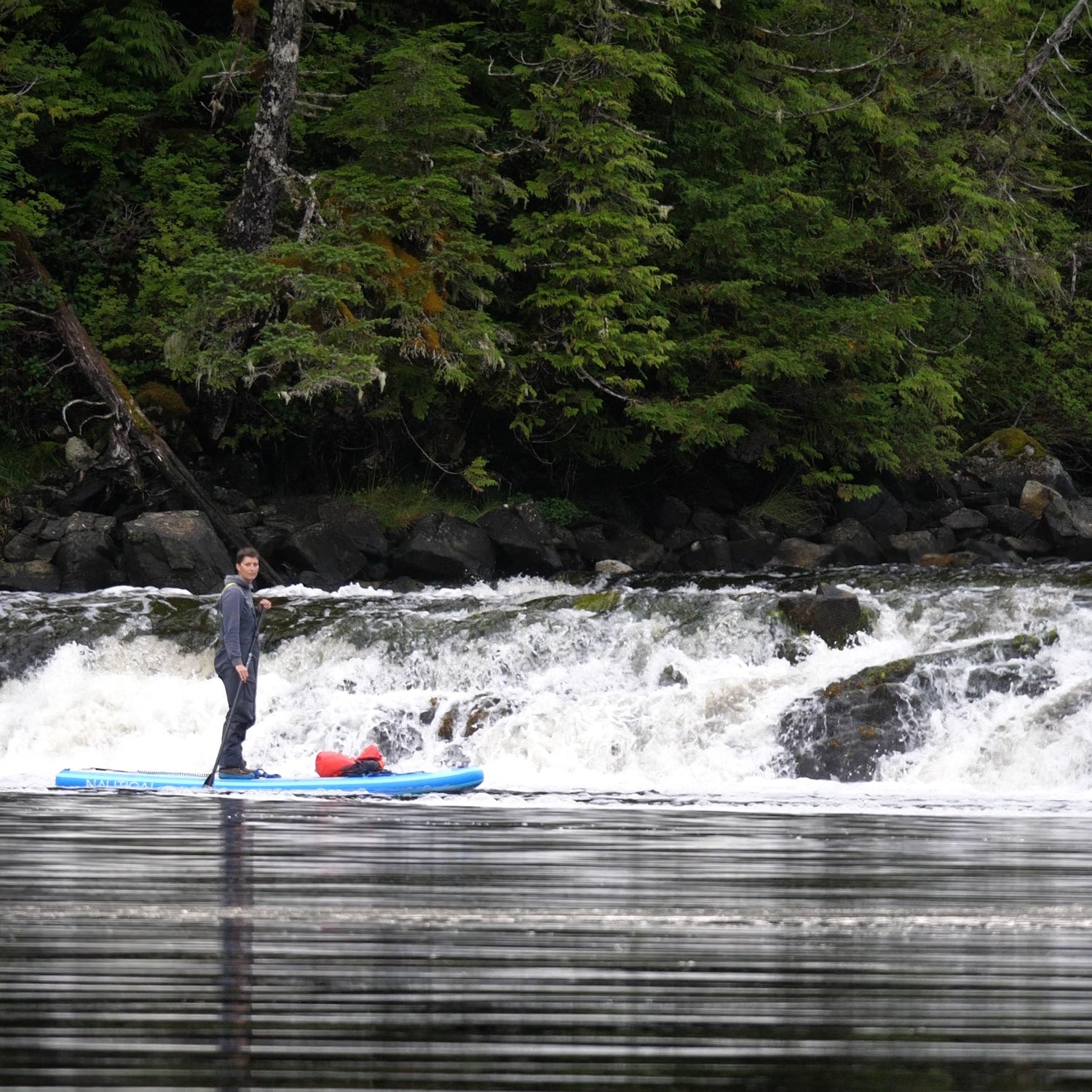 Person paddleboarding in Haida Gwaii British Columbia Canada on a river with a waterfall and forest in the background