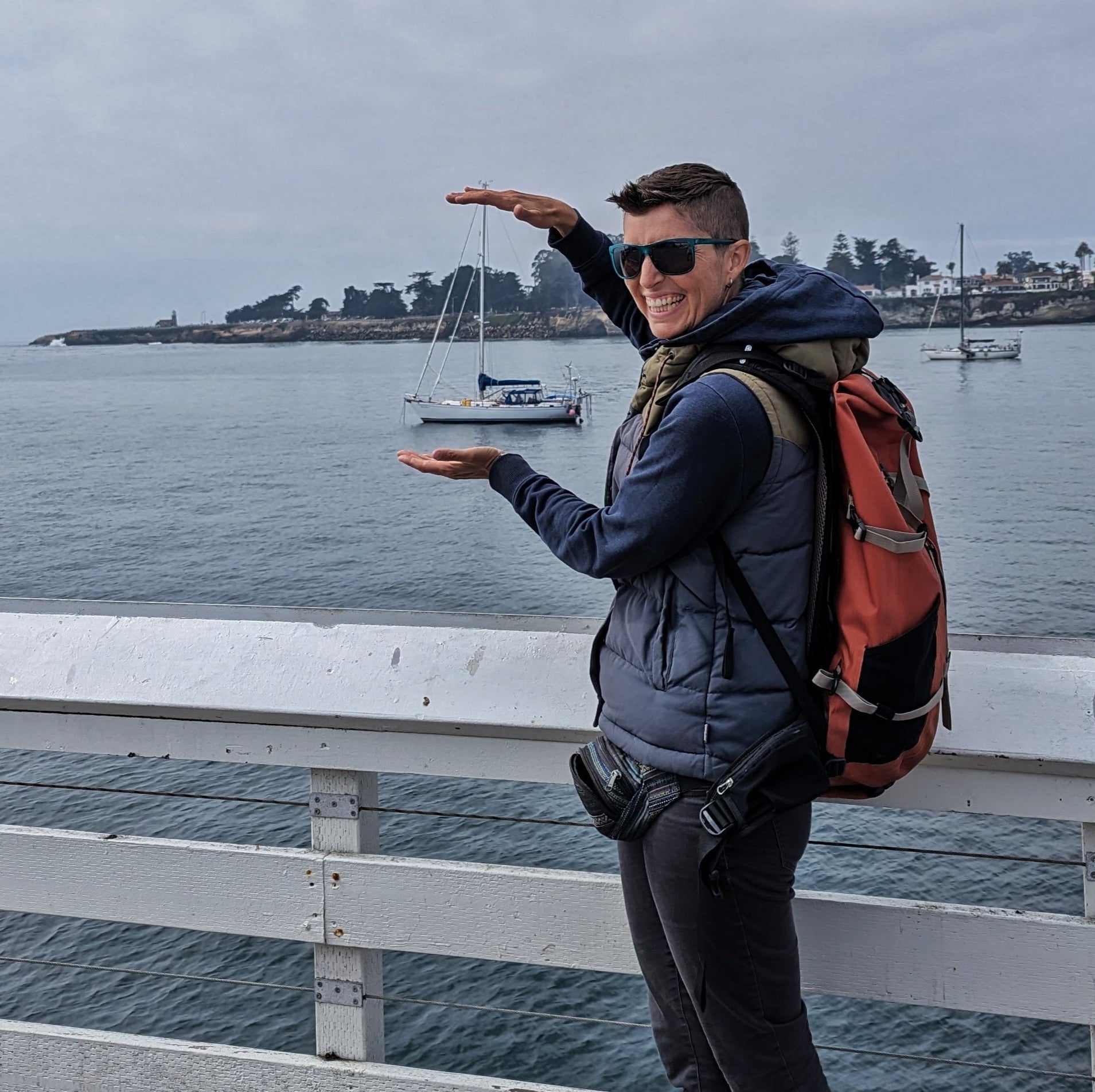 A person standing on a pier trying to look like they are holding a far off boat between their hands