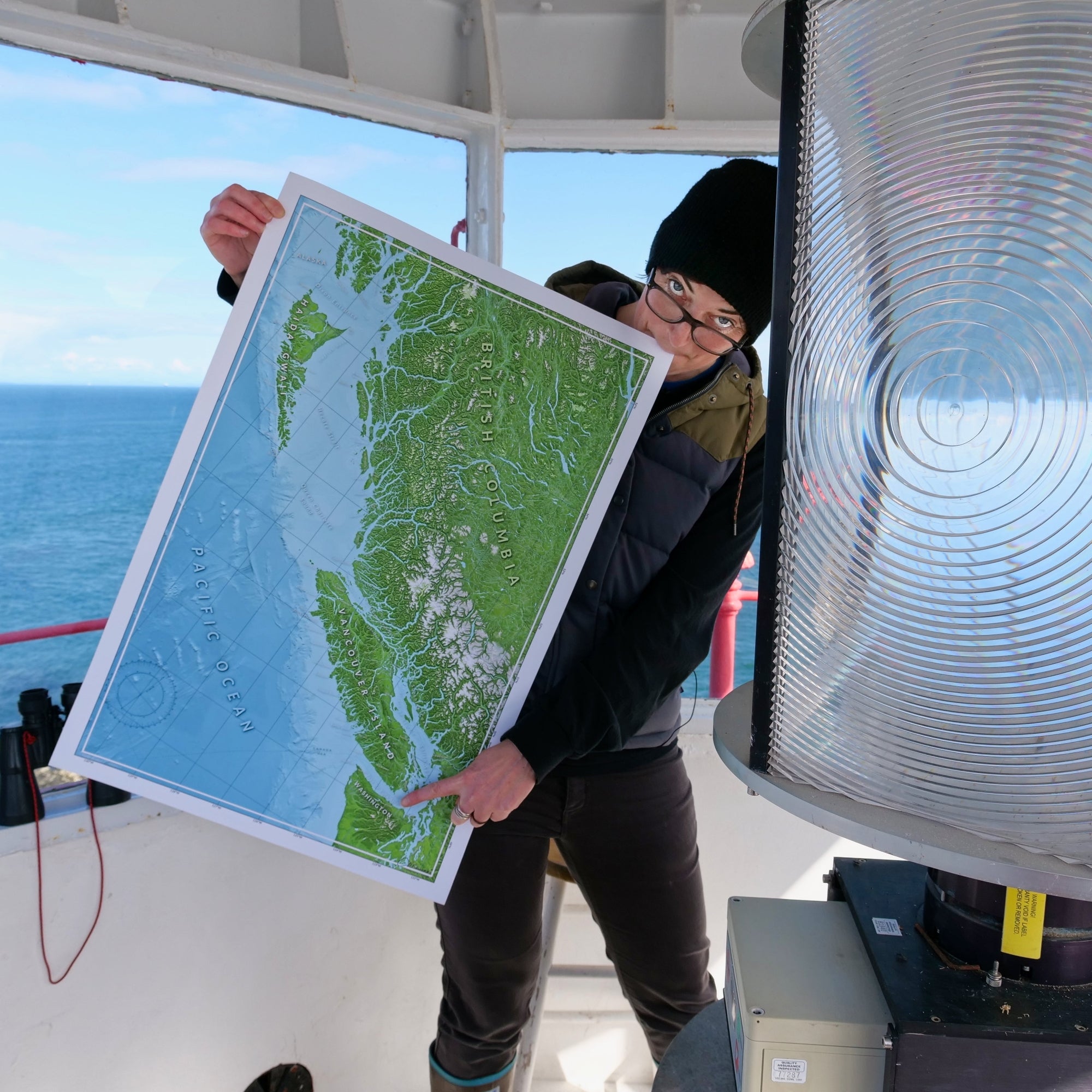 Person holding a map of a coastal British Columbia at the top of a lighthouse with an ocean view behind them