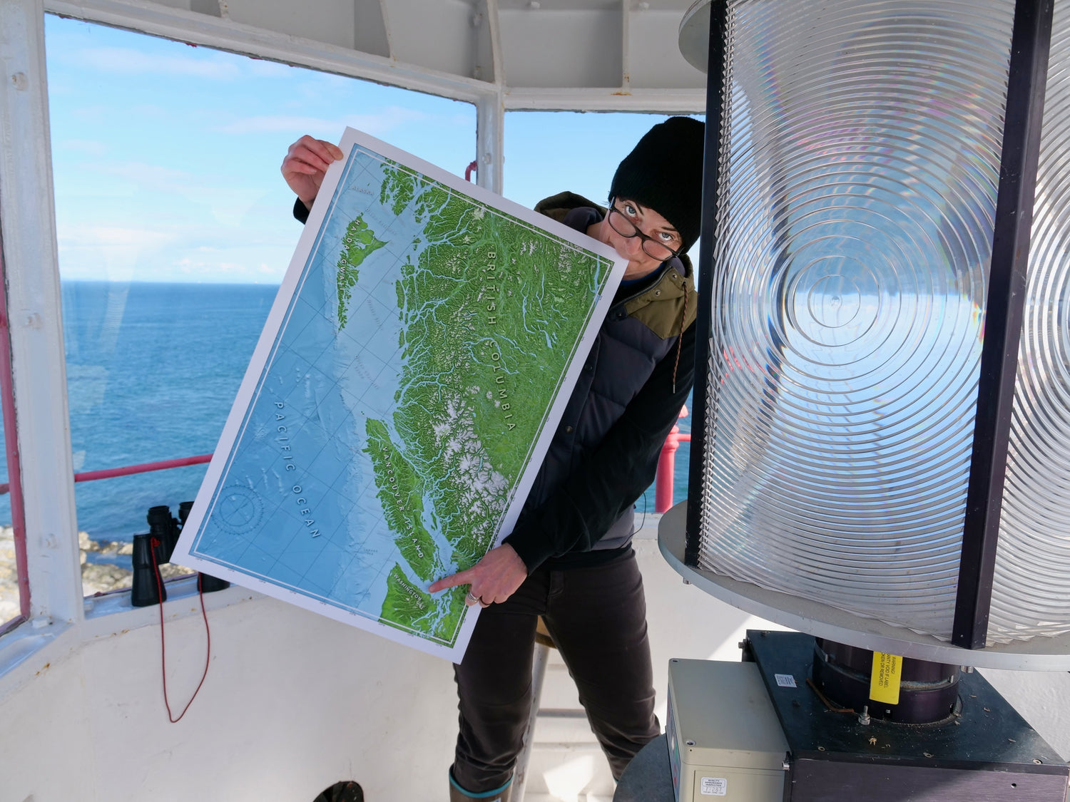 Person holding a map of a coastal British Columbia at the top of a lighthouse with an ocean view behind them