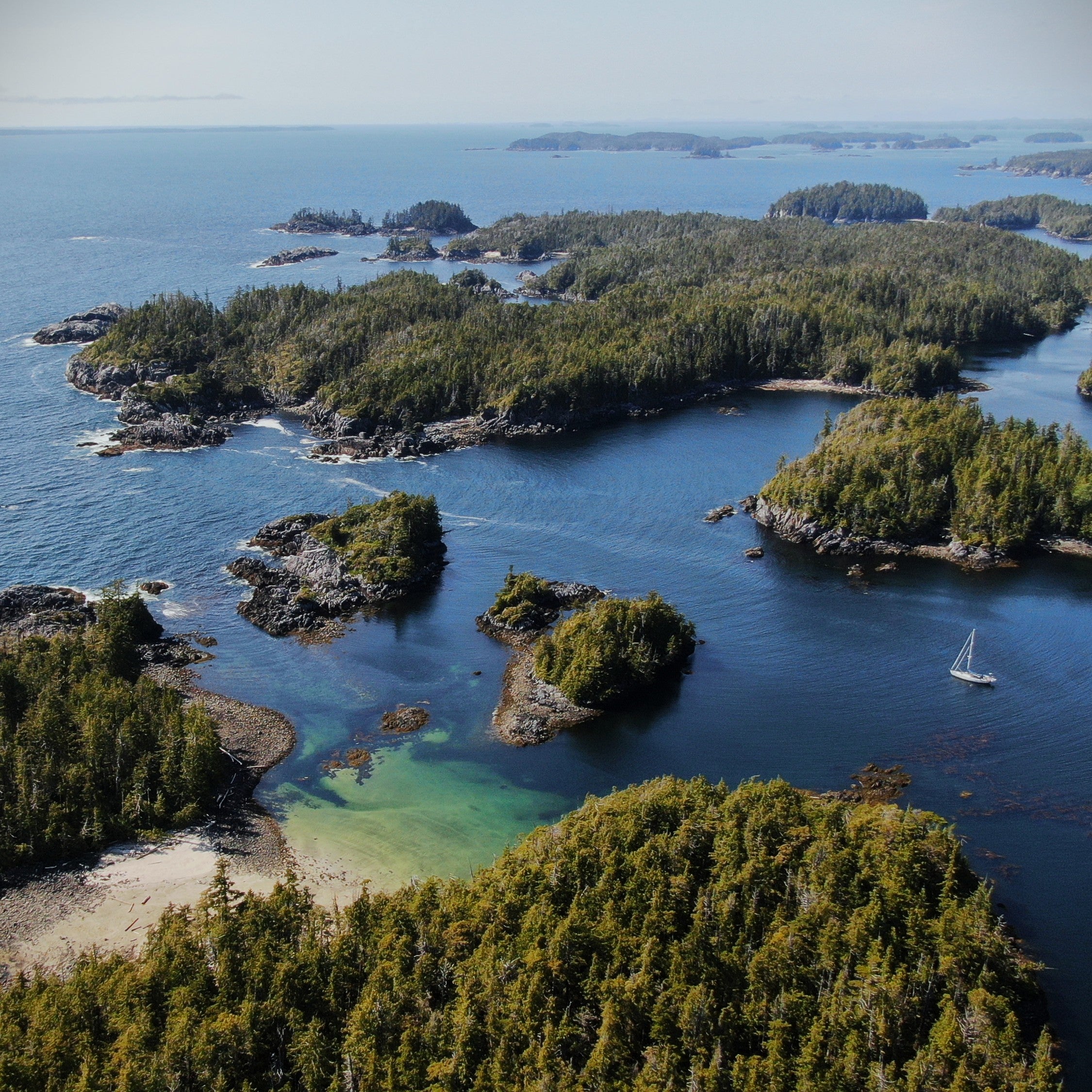Many small islands on the west coast of British Columbia surrounded by water with a sailboat anchored in the distance