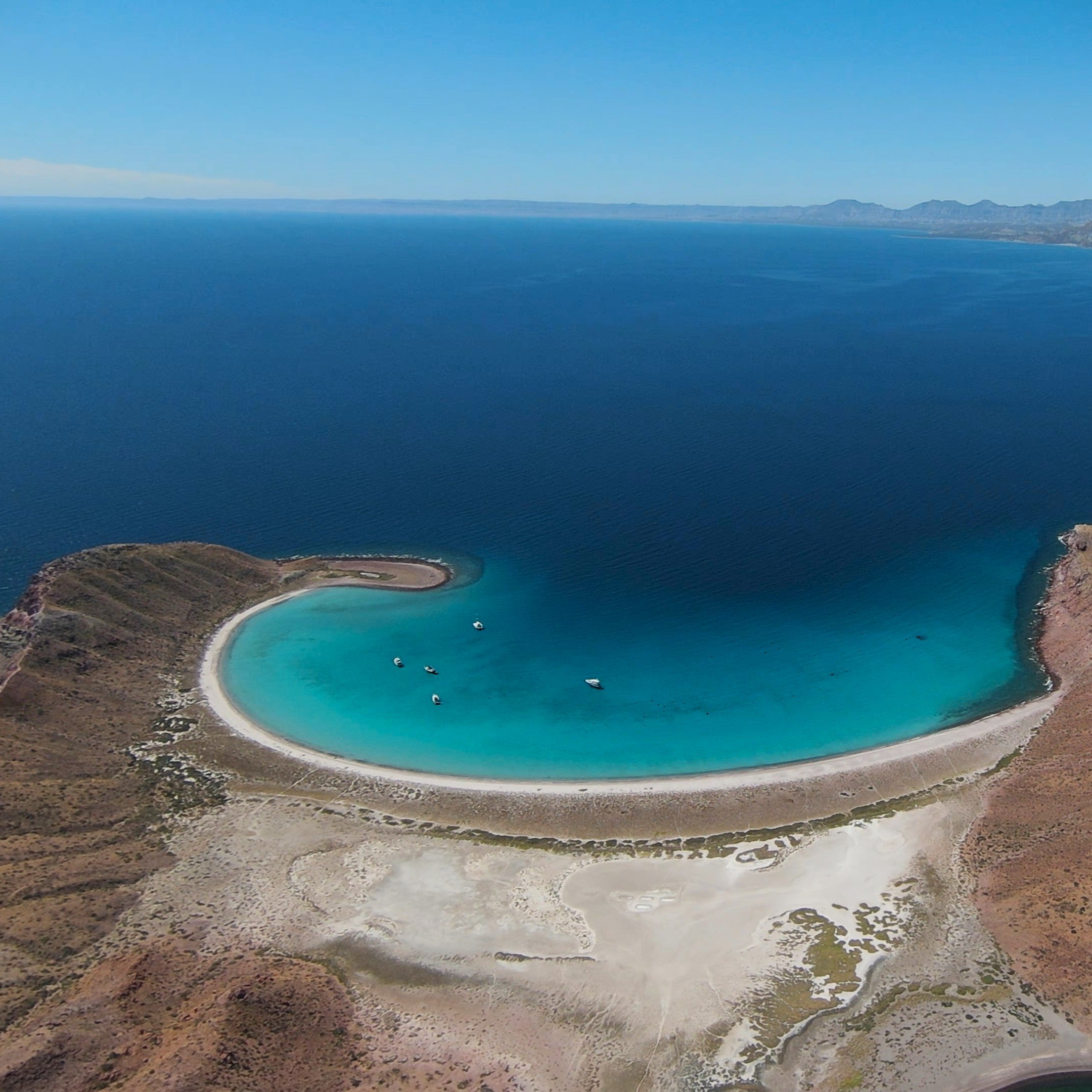 Aerial view of a desert island in Baja Sea of Cortez with a lagoon and clear blue water and boats anchored