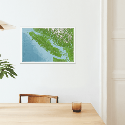 A printed map poster for wall art of Vancouver Island displayed, with various shades of green and blue representing land and water features. Hanging in a minimalist dinning room.