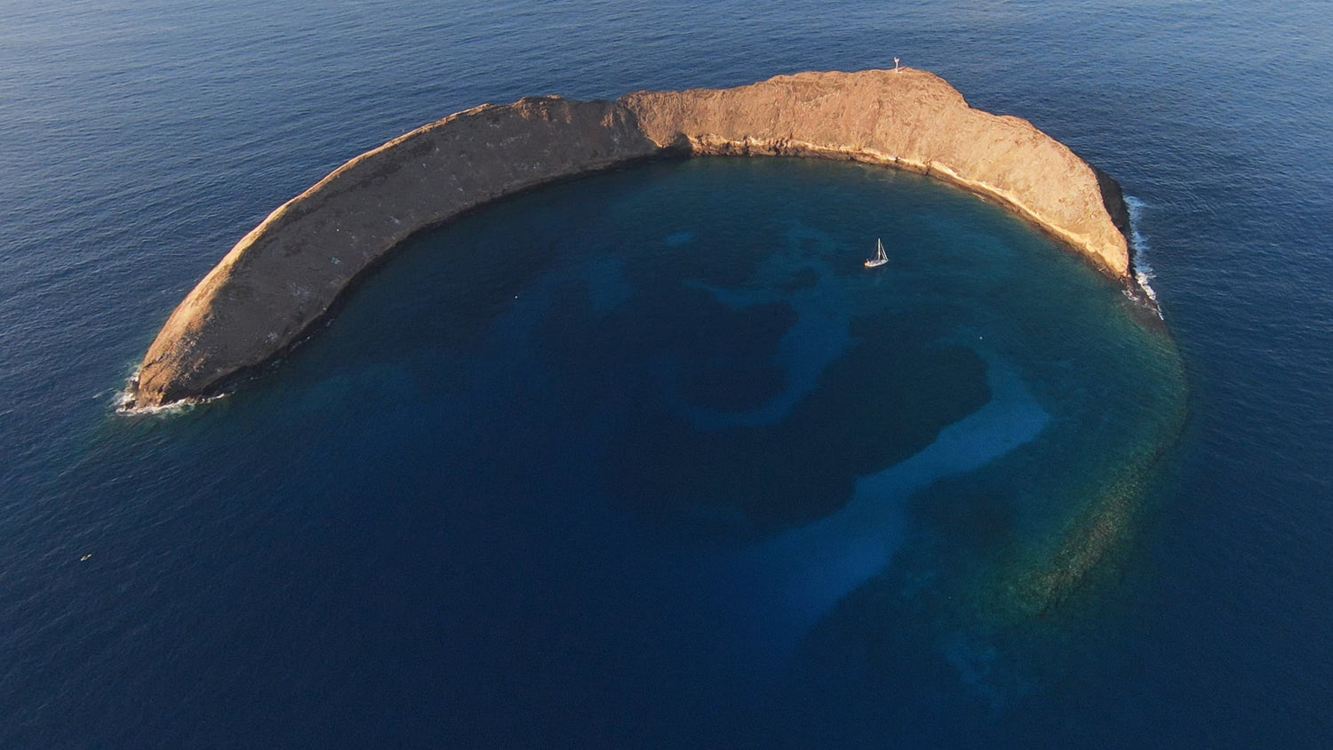 Aerial view of the Molokini crater in Haiwaii, with a boat near anchored in the middle of the ocean.