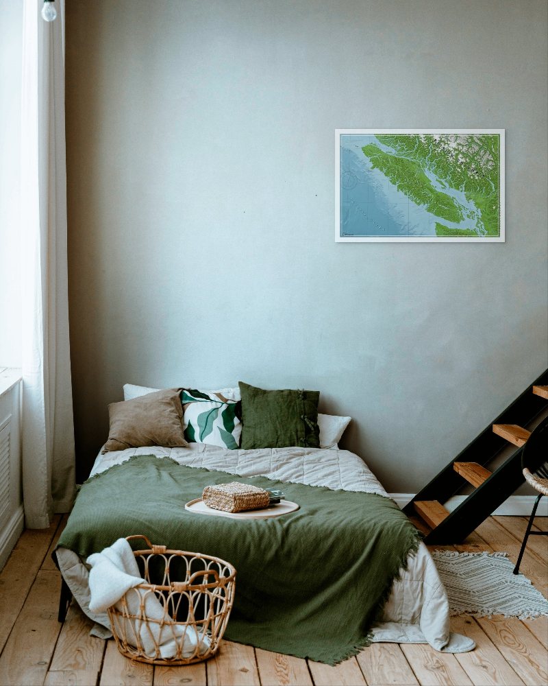 Cozy bedroom with a bed, green blanket, and wall art of a map of Vancouver Island and the lower mainland.