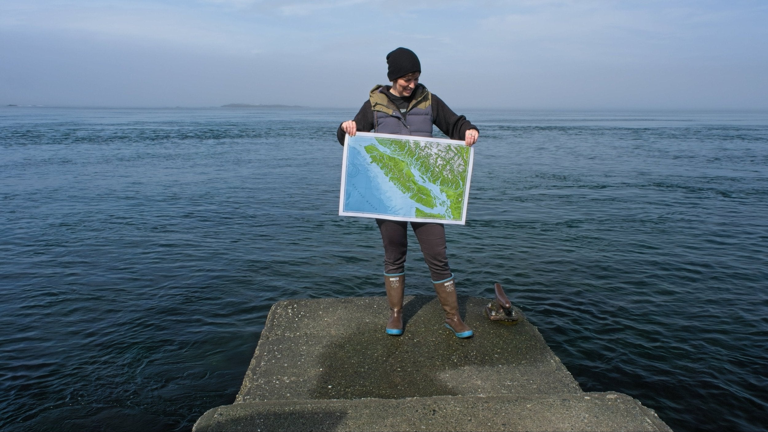 Marine cartographer standing on a concrete jetty holding a map of Vancouver Island
